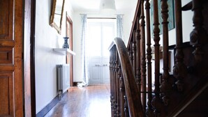 A wooden staircase with a handrail leading to a white door. A radiator is visible on the wall to the left, and a blue vase is on a shelf above the door.