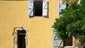 A building with a yellow facade, a stone entrance, and shutters on the windows.
