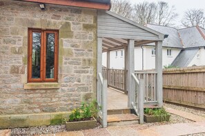 Une maison en pierre avec un porche en bois et un petit jardin.