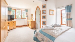 A bedroom with a bed, a dresser, a TV, a window, and a door. - Duporth Lodge - Three Bedroom Cottage, Sleeps 6 (Charlestown)