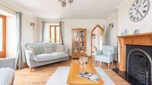 A living room with a sofa, armchairs, a wooden coffee table, a fireplace, and a large wall clock. - Duporth Lodge - Three Bedroom Cottage, Sleeps 6 (Charlestown)