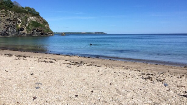 A beach with a rocky cliff and calm sea. - Duporth Lodge - Three Bedroom Cottage, Sleeps 6 (Charlestown)