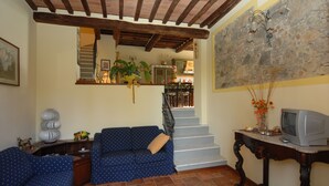 A living room with a blue sofa, a wooden table with a television, and a staircase leading to a kitchen.