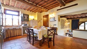 A rustic kitchen with a dining table set for breakfast, wooden beams on the ceiling, and a stone wall.