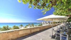 Eine Terrasse am Meer mit Sitzgelegenheiten im Freien und Blick auf den Ozean, im Hintergrund ein Gebäude.