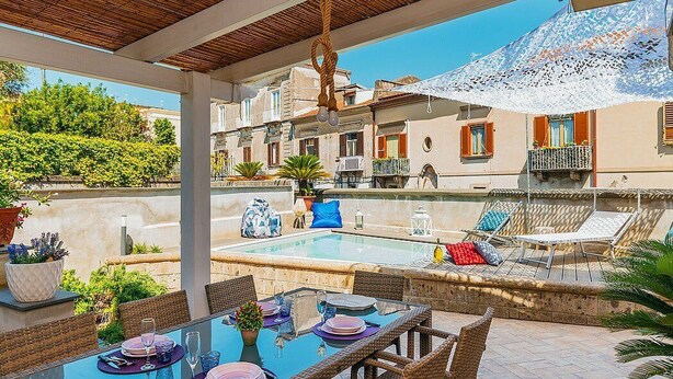A covered outdoor dining area with a pool, wicker furniture, and a view of buildings in the background. - Villa Mira: An elegant and welcoming three-story villa located in the center of Sant'Agnello, with Free WI-FI. (Sant'Agnello)