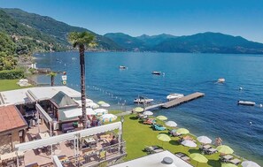 A lakeside resort with a dock, boats, and a grassy area with umbrellas. - 1 bedroom gorgeous apartment in Oggebbio (VB) (Oggebbio (VB))