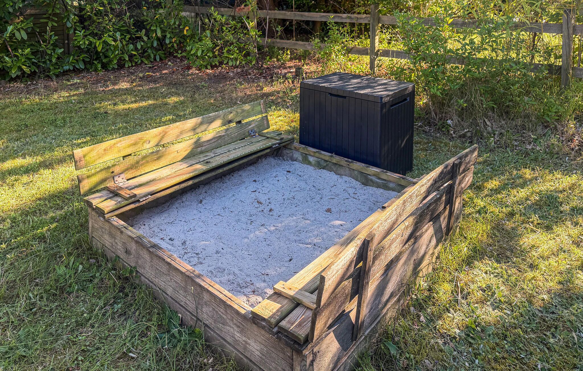 A wooden compost bin with a lid, surrounded by grass and a wooden fence.