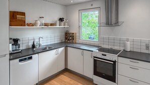 Een moderne keuken met witte kasten, een zwart aanrecht, een inbouwoven en een raam met uitzicht op groen.