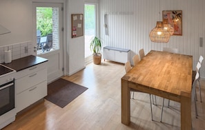 A modern kitchen with white cabinetry, a wooden dining table, and a hanging light fixture.