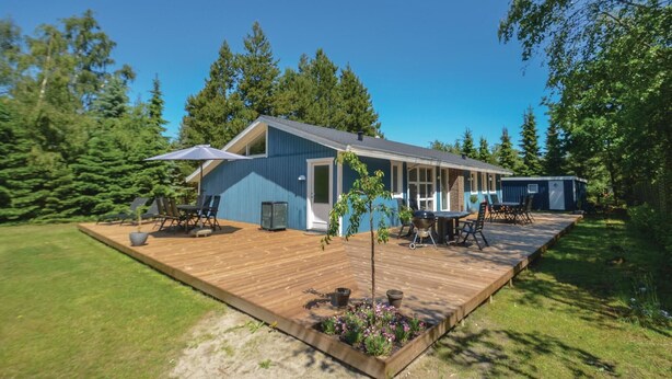 Een blauwe blokhut met een houten terras, buitenmeubels en een kleine tuin.