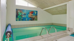 Een binnenzwembad met een muurschildering, een duikplank en een betegelde vloer.