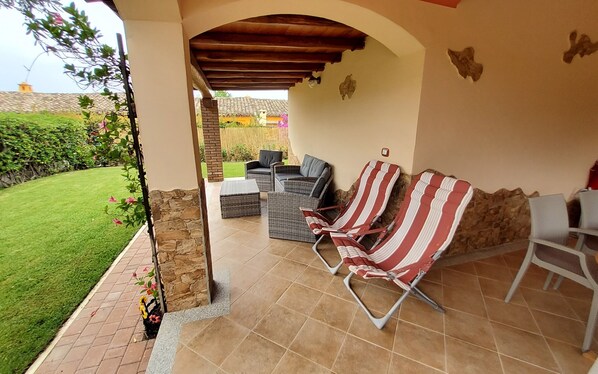 Un patio al aire libre con mobiliario de mimbre, un muro de piedra y vistas a un jardín.