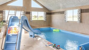 Una piscina interior con tobogán, una escalera y un flotador inflable verde.