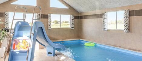 An indoor swimming pool with a slide, a ladder, and a green inflatable ring.