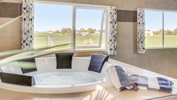 Un baño moderno con una bañera grande, dos ventanas con cortinas estampadas y vistas a un paisaje verde.