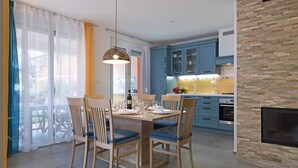 A modern kitchen with blue cabinets, a stone accent wall, and a dining area with wooden chairs and a table set for four.