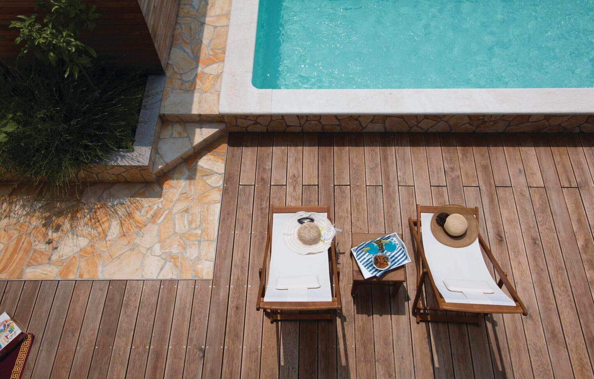 Una terraza de madera con dos tumbonas, una piscina y paredes de piedra.