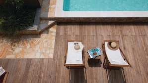 A wooden deck with two sun loungers, a pool, and stone walls.