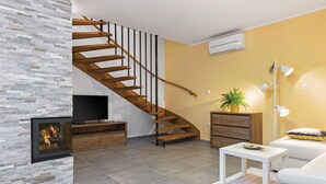 A modern living room with a wooden staircase, a flat-screen TV, a fireplace, a sofa, a coffee table, and a potted plant.