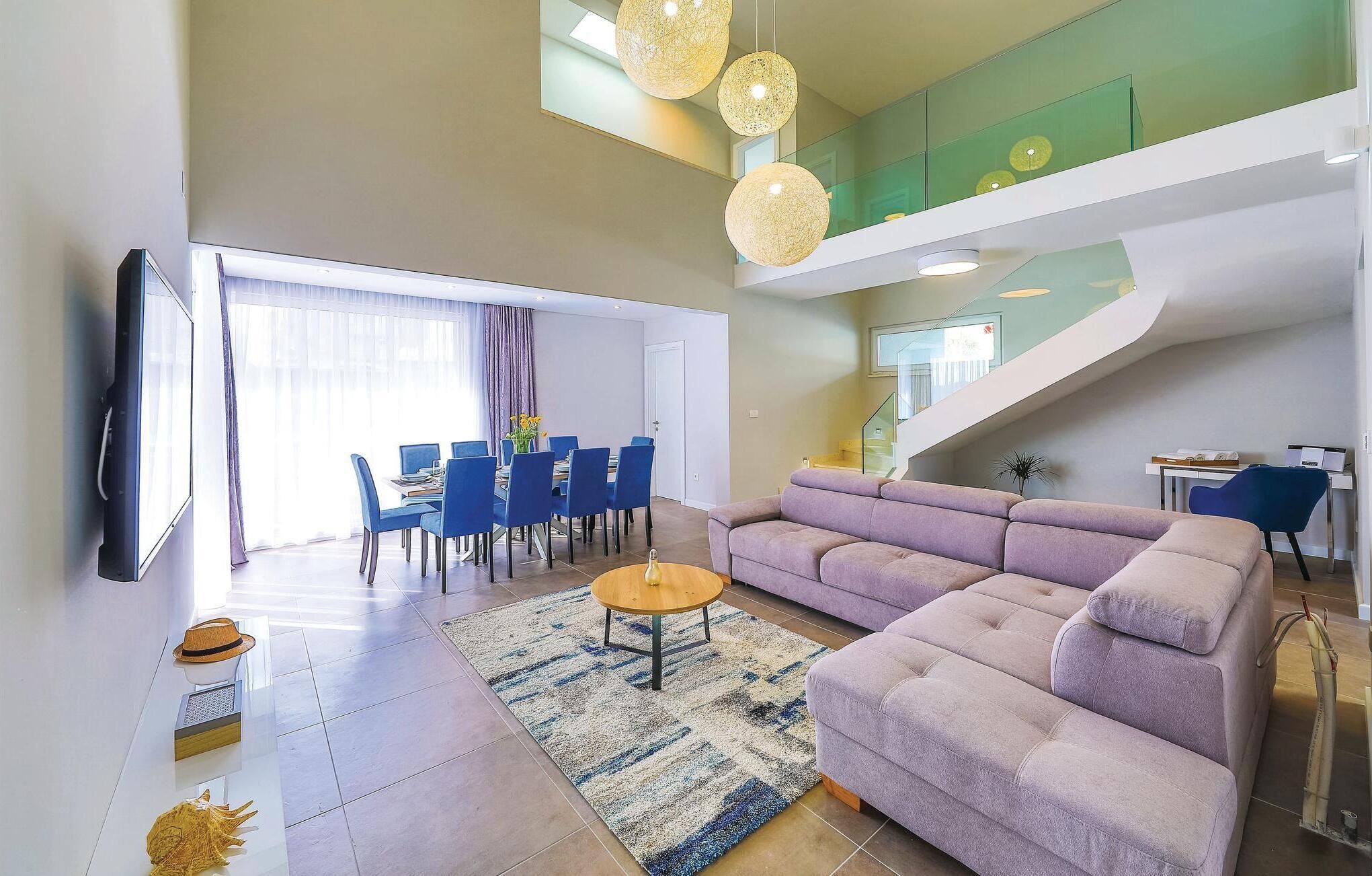 A modern living room with a large sofa, a coffee table, and a dining area with blue chairs.