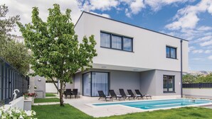 Et moderne hus med to etager, en swimmingpool, et spiseområde og et træ i forhaven.