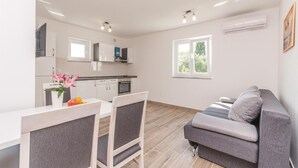 A modern kitchen with white cabinets, a dining area with a table and chairs, and a gray sofa in a living area with a window. - 1 bedroom stunning apartment in Biograd na Moru (Biograd na Moru)