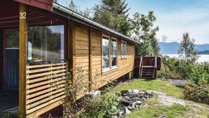Eine Holzhütte mit der Nummer 32, großen Fenstern, einer Terrasse und Blick auf einen See und Berge.