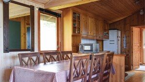 Ein Holzblock-Interieur mit Esstisch, Stühlen, einer Küchenzeile inklusive Mikrowelle und Kühlschrank.
