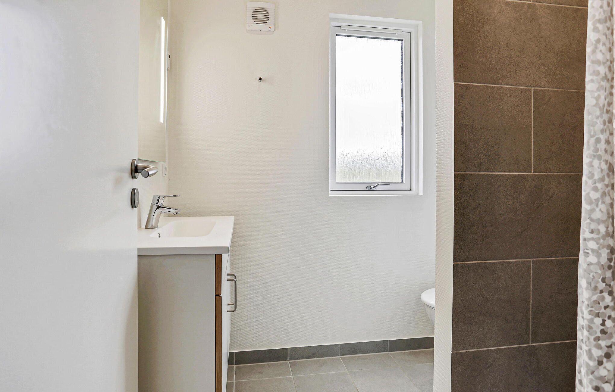 A bathroom with a white sink, a mirror, and a window.