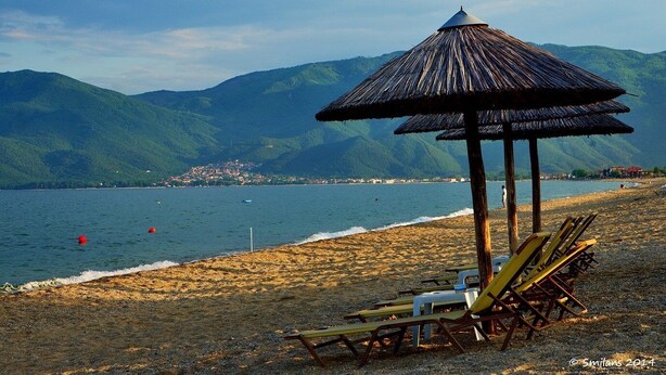 A beach with a thatched-roof pavilion, lounge chairs, and a view of mountains and a lake. - Luxury Traditional Stone House in Vrasna (Vrasna)
