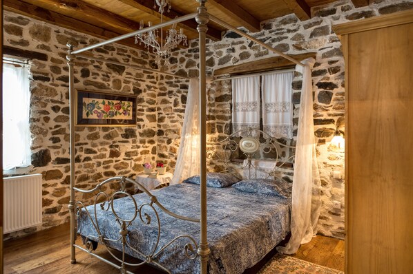 A stone-walled bedroom with a four-poster bed, a chandelier, and a wooden ceiling.