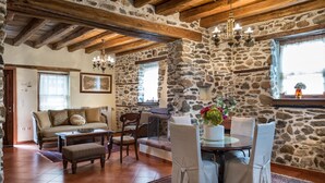 A rustic stone-walled room with a wooden ceiling, a sofa, a dining table with chairs, and a chandelier. - Luxury Traditional Stone House in Vrasna (Vrasna)