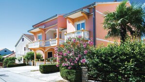 Ein zweistöckiges Haus mit Balkon, umgeben von viel Grün und blauem Himmel.