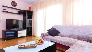 Ein Wohnzimmer mit einer Couch, einem Couchtisch mit Obst und Nüssen, einem Fernseher und einem Bücherregal.