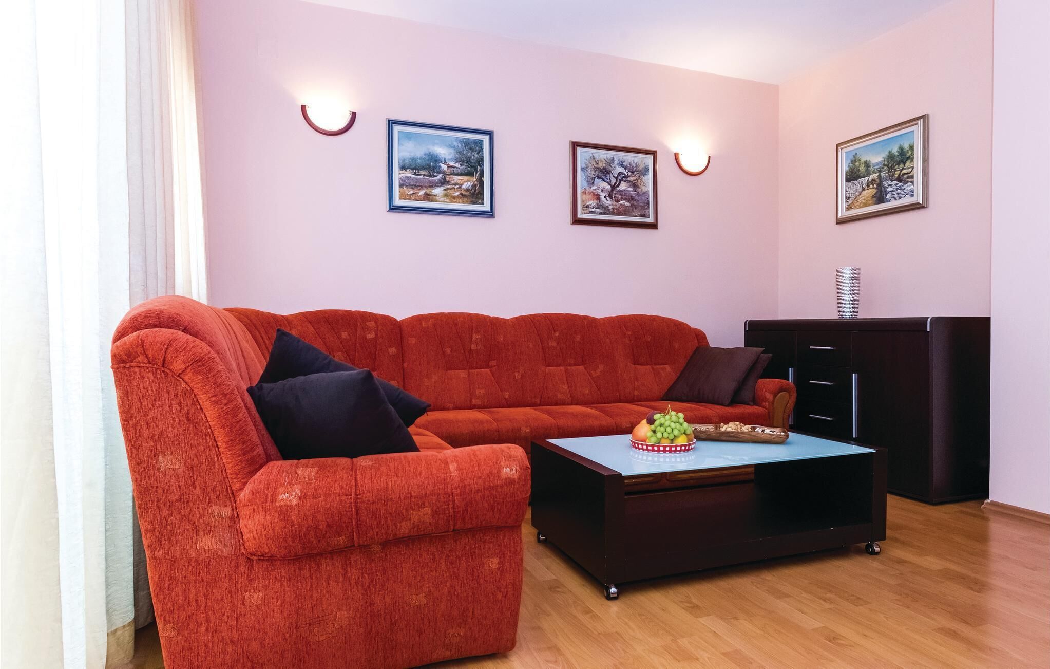 Una sala de estar con un sofá rojo, una mesa de centro con fruta y tres cuadros en la pared.