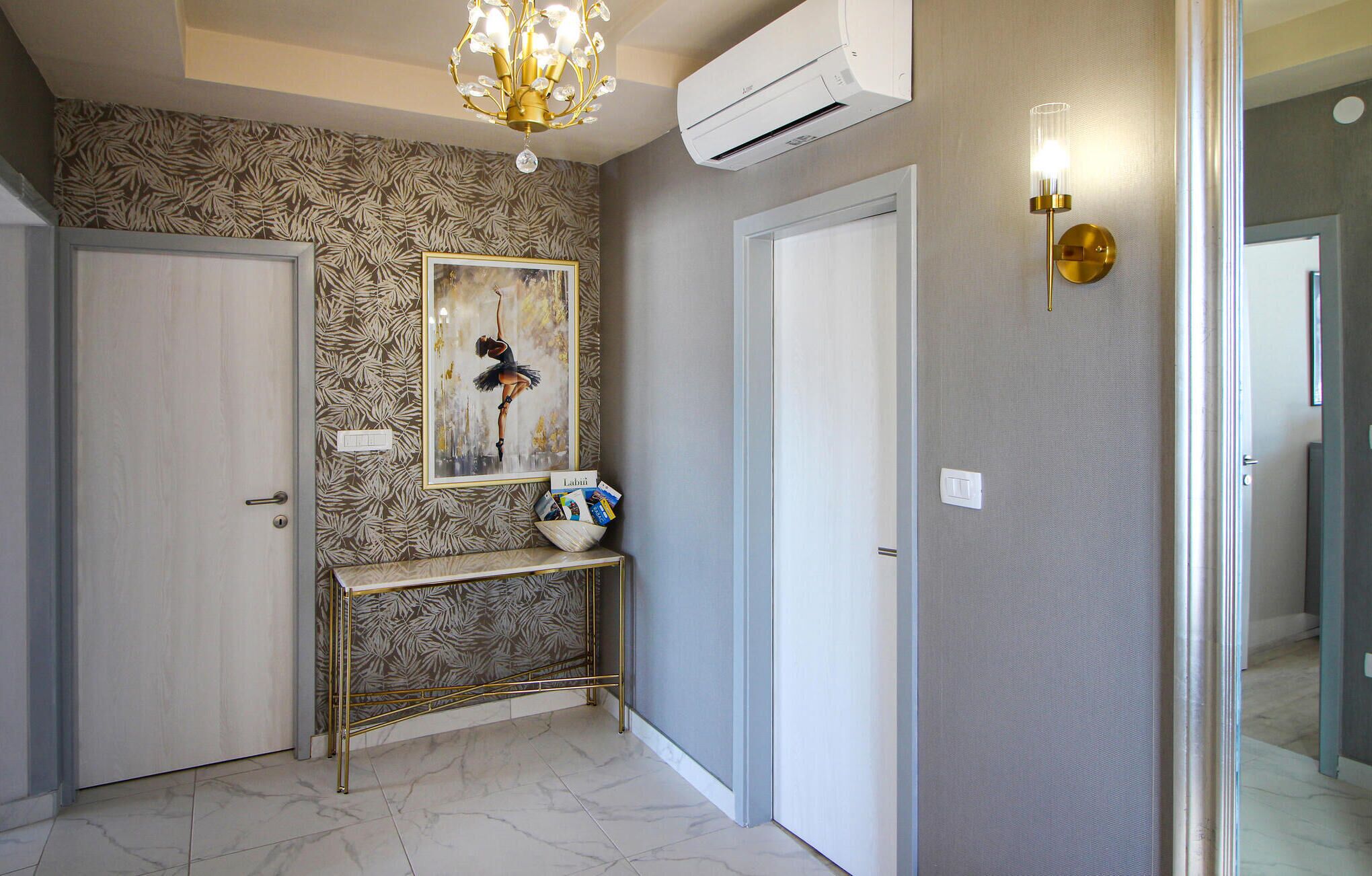 A hallway with patterned wallpaper, a ballet dancer painting, a gold console table, and an air conditioning unit.