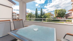 Een balkon met een metalen tafel en stoelen, een helder uitzicht op de lucht en omliggende gebouwen.