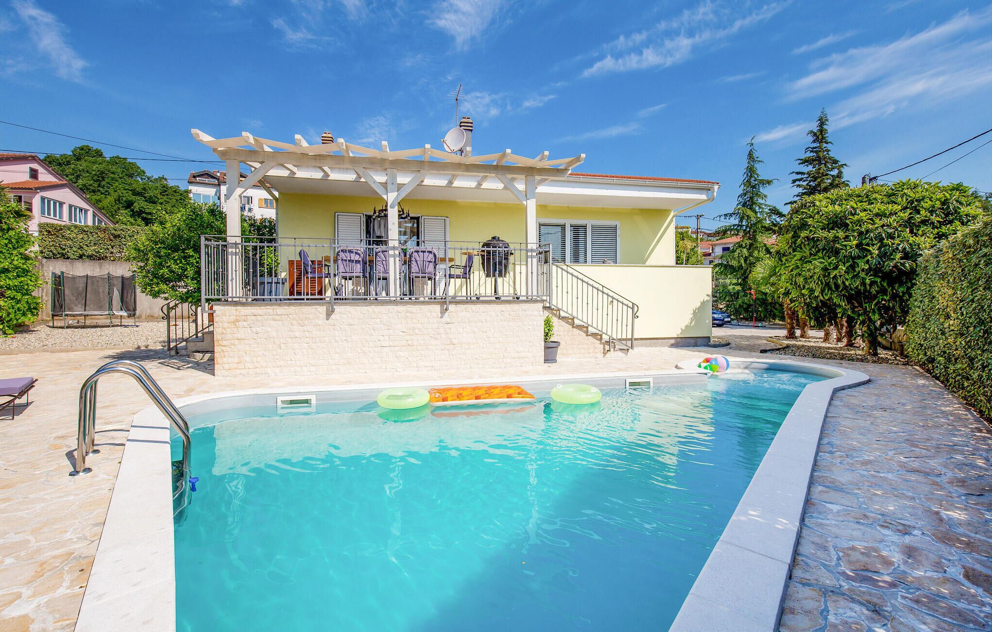 A swimming pool with a sun terrace, a covered seating area, and a view of the surrounding neighborhood.