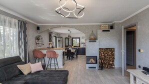 A modern living room with a sofa, a dining area with a kitchen in the background, and a fireplace with wood logs. - Stunning home in Opatija with sauna (Opatija)