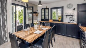A modern kitchen with dark cabinetry, a wooden dining table, and a clock on the wall. - Stunning home in Opatija with sauna (Opatija)