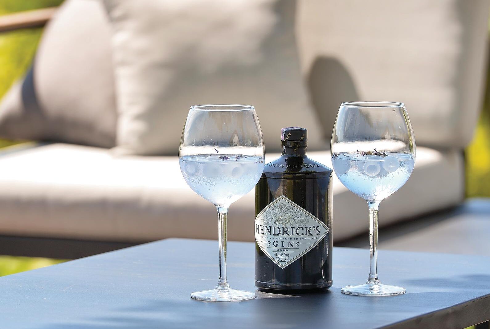 Una botella de ginebra Hendrick's y dos vasos de ginebra sobre una mesa.