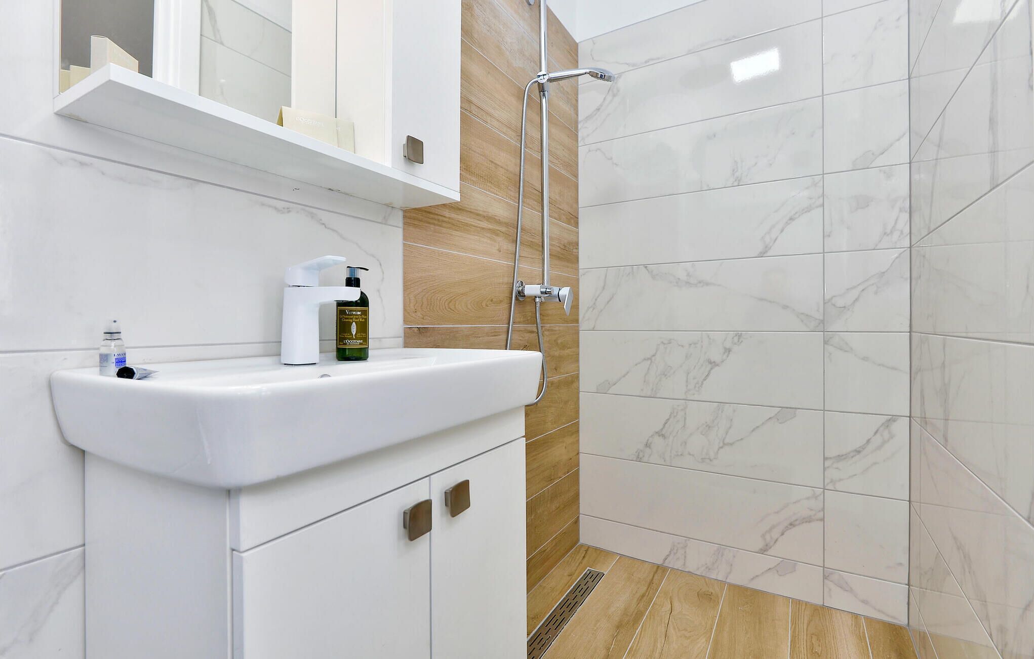 Un baño moderno con lavamanos blanco, ducha de mano y tocador de madera.