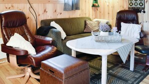 Ein gemütliches Wohnzimmer mit einem grünen Sofa, zwei Ledersesseln, einem kleinen weißen Tisch mit einem Korb und einem gemusterten Teppich.