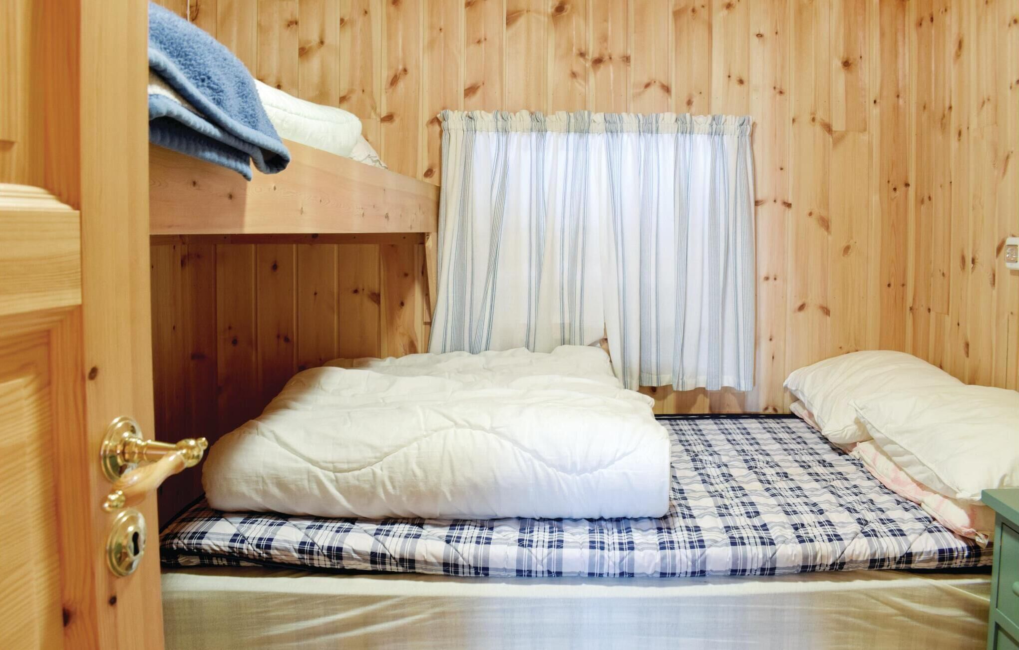 A bunk bed room with a window covered by curtains, a wooden door, and a bedside table.