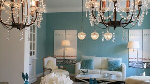 Una sala de estar con pared verde azulada, sofá blanco y una araña.