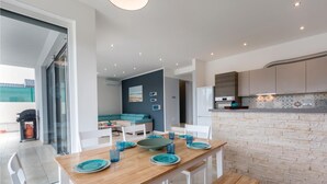 Een moderne keuken met een betegelde muur, een eethoek met een houten tafel en blauwe borden, en een zithoek met een bank en een schilderij.