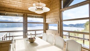 A wooden cabin with a dining table and chairs, large windows with a view of a lake and mountains. - Lovely home in Norheimsund with WiFi (Norheimsund)