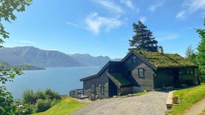 A cabin with a sloped roof, a small porch, and a view of a lake and mountains. - Lovely home in Norheimsund with WiFi (Norheimsund)