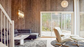 Un salon moderne avec un mur en bois, une grande fenêtre, un canapé gris, un fauteuil blanc et un luminaire suspendu.